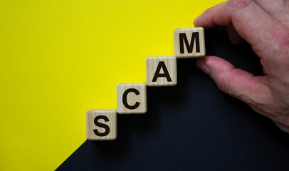 Wood cubes with word 'scam' stacking as step stair on paper black and yellow background, copy space. Male hand. Concept.