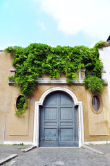 Fototapeta na wymiar Old blue vintage door in Italy. Blue sky above and green plant lingering on the facade.