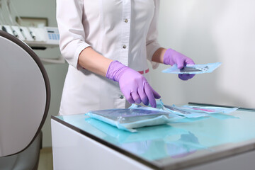 A nurse in a uniform and medical mask lays out sterile dental instruments Packed in a Kraft bag. Unrecognizable photo.Gloved hand. Copy of the space. Gray background.