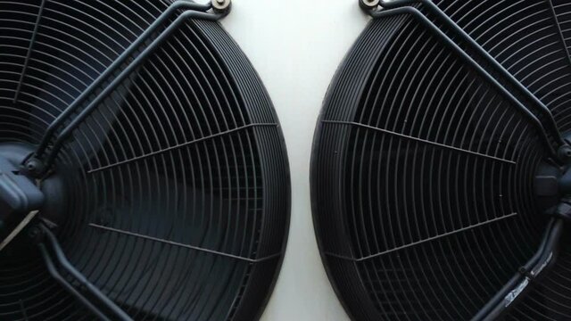 Panning shot of two large industrial air conditioning condenser fans slowly rotating