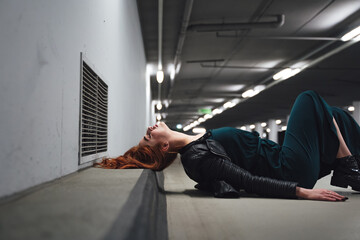 Millennial girl with head tilted back laying on floor in parking house. Female model red hairs...
