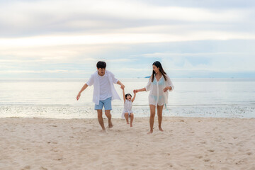 Fototapeta na wymiar Happy Asian family holidays during joyful father, mother and daughter running together along summer sunset sea. Happy family travel on beach in holiday, Summer and vacation.