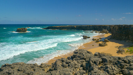 Foaming ocean waves wash the small sandy bay surrounded by rugged rocky cliffs