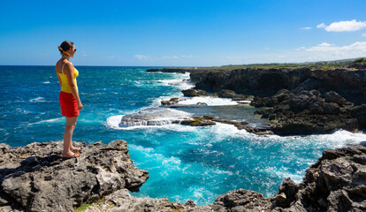 COPY SPACE: Female traveler stands on the edge of a cliff and observes the coast - obrazy, fototapety, plakaty