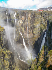 Beautiful landscape. Waterfall falls from a cliff into an abyss and small house on a precipice. Norway.