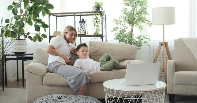 Mother having fun tickling her son while watching movie on laptop at home