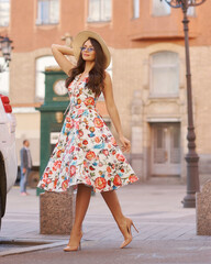 Young woman in colorful dress walking city street on a sunny summer day. Full length portrait. Elegant lady with long wavy hair. Girl in sunglasses