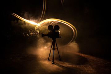 Movie concept. Miniature movie set on dark toned background with fog and empty space. Silhouette of vintage camera on tripod.
