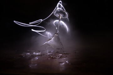 Broken glasses on wooden table at dark toned background with fog. Selective focus
