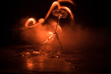 Broken glasses on wooden table at dark toned background with fog. Selective focus