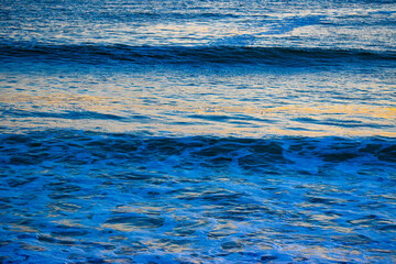 Sapphire sea waves with reflecting sunset yellow light shone down