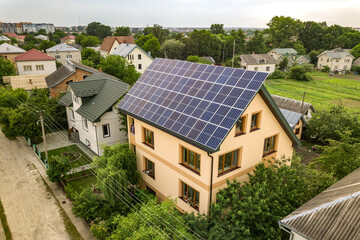 Aerial top view of new modern residential house cottage with blue shiny solar photo voltaic panels system on roof. Renewable ecological green energy production concept.