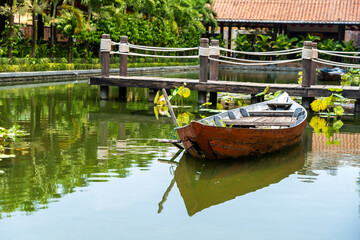 Obraz premium Wooden boat on the pond near the pier in a tropical garden in Danang, Vietnam