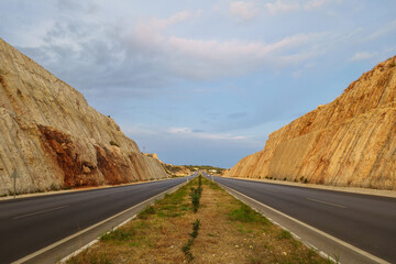 View onto highway and dividing strip passing in a mountain or hilly area. There is a steeply cut hill on both sides of the road