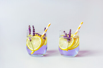Glasses with lavender lemonade with yellow straws, grey background, close up