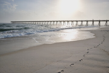 Footprints in sand lead to Pensacola Pier; misty winter morning