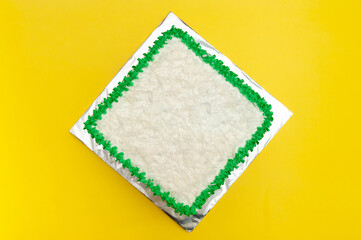 Birthday cake decorated with green icing and grated coconut. Isolated on yellow background. Top...