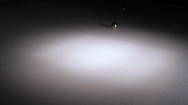 Steel ball bearings drop onto bouncy white surface, concept of kinetic energy and surface tension.