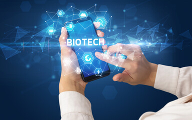 Female hand holding smartphone with BIOTECH inscription, modern technology concept