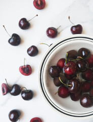 Whole and halved cherries on white surface and in bowl with water