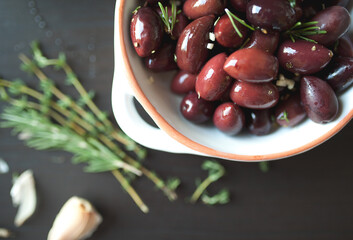 Overhead shot of seasoned kalamata olives in white dish with herbs and garlic on dark background