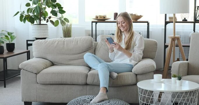 Woman having fun text messaging using mobile phone on sofa at home