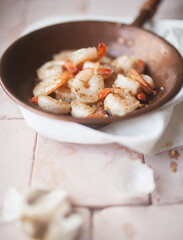 Garlic and butter shrimp in copper pan with linen on blush tile surface