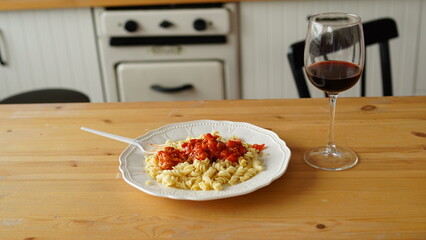 Close up of dish in white plate with glass of wine on table in kitchen.