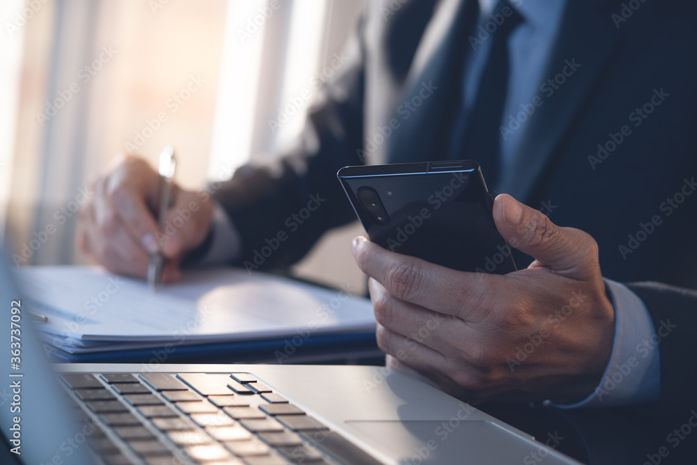 Poster businessman working in modern office and using mobile phone with laptop computer on table