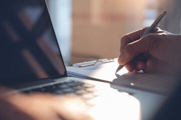 close up of man hand writing on paper document while working on laptop computer in office