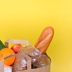 Paper bag with food supplies for the period of quarantine isolation on a yellow background. Food delivery, donation, coronavirus. Copyspace.