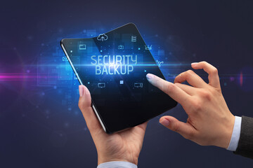 Businessman holding a foldable smartphone with SECURITY BACKUP inscription, cyber security concept