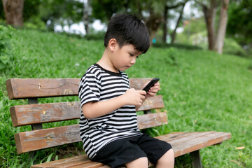 Cute little boy sitting on a park bench and playing with mobile phone