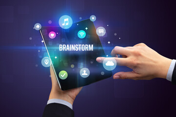 Businessman holding a foldable smartphone with BRAINSTORM inscription, social media concept