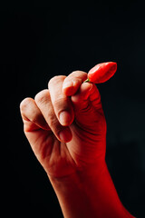 Isolated unrecognizable woman's hand holding a red habanero pepper on a black background.
