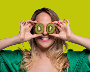 Happy and smiling young woman playing with a cut of Kiwi fruit in half and in front of her eyes....