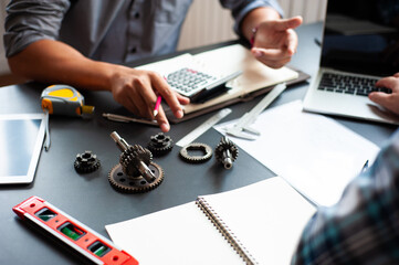 Two engineers work at the desk and discuss the design of the engine interior parts.