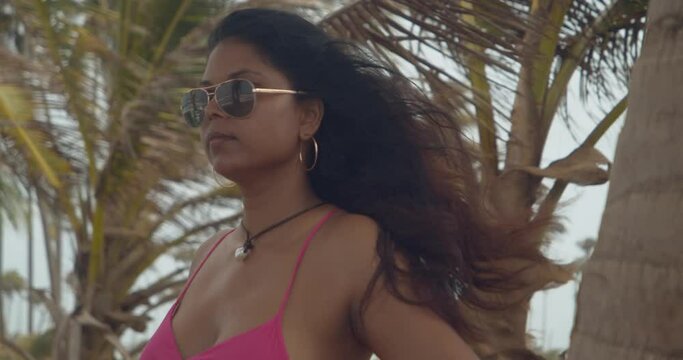 An Indian model with long hair flowing in the wind and coconut trees swying in the background