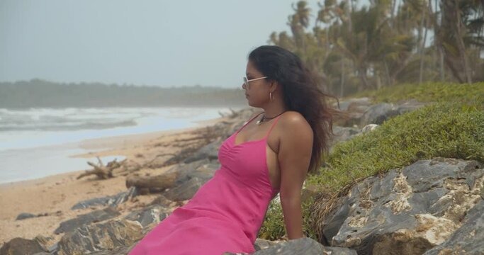 Sexy Indian model sits on the rocks of this coastline with waves crashing at the shoreline in slowmotion
