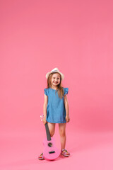 cheerful little girl in a hat poses with a ukulele guitar on a pink background.