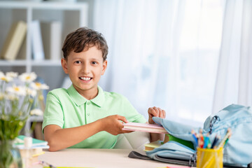 Cute happy schoolboy puts office supplies in a backpack. Preparation for school.
