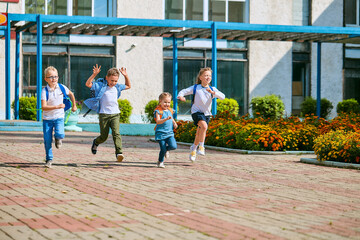 group of school children with backpacks run out of school, after the end of classes.