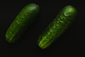 Two green cucumbers on a black background, close up.