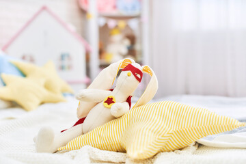 Fototapeta na wymiar plush rabbit handmade from fabric in a superhero costume sits in children room.