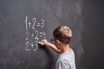 Primary education. Side view a student solves a math example on a blackboard.