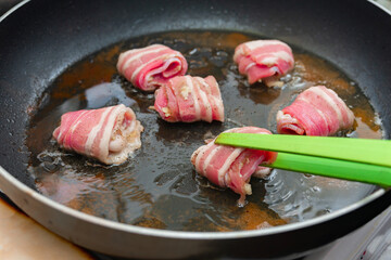Raw rolls with bacon are fried in a pan. Cooking junk and fatty foods.