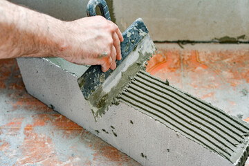 A worker applies adhesive mortar to a wall block in a private house. Foam masonry, repair and construction.