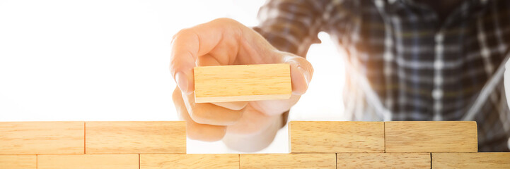 Hand of engineer playing a blocks wood tower game on blueprint or architectural project.