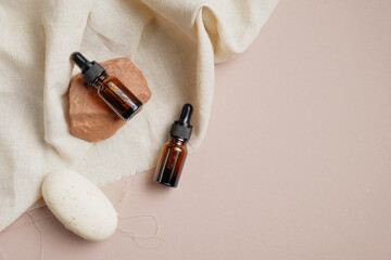 Amber glass dropper bottles with serum hair oil and natural soap on beige background. Flat lay, top view, overhead.