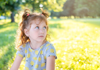 Beautiful little girl in the Park at sunset. A young girl is upset looking away. Little toddler girl in a t-shirt in meadow at sunset with yellow background